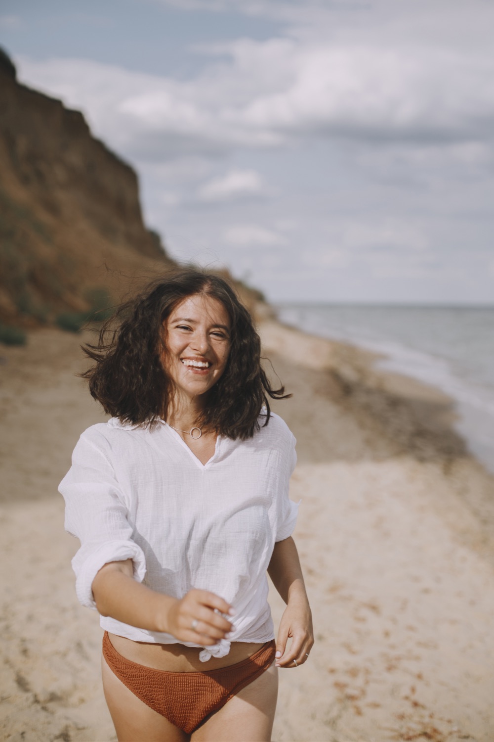 A smiling woman in a white shirt running along the beach.